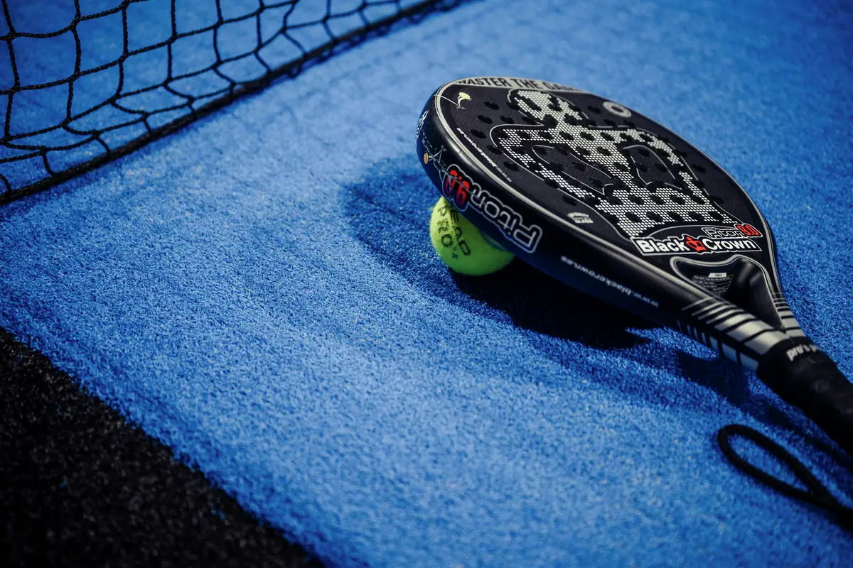 Padel-Racket und Ball liegen am Netz auf dem blauen Court im Padelhouse