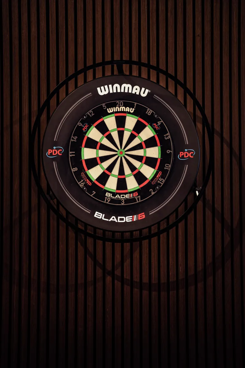 Dartscheibe mit Beleuchtungsring an der Holzlamellenwand auf der Galerie