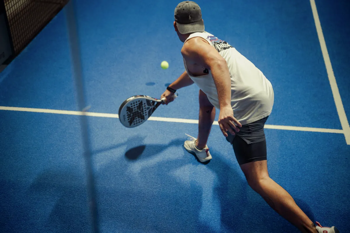 Padel-Spieler schlägt im Padelhouse eine Rückhand auf dem blauen Court