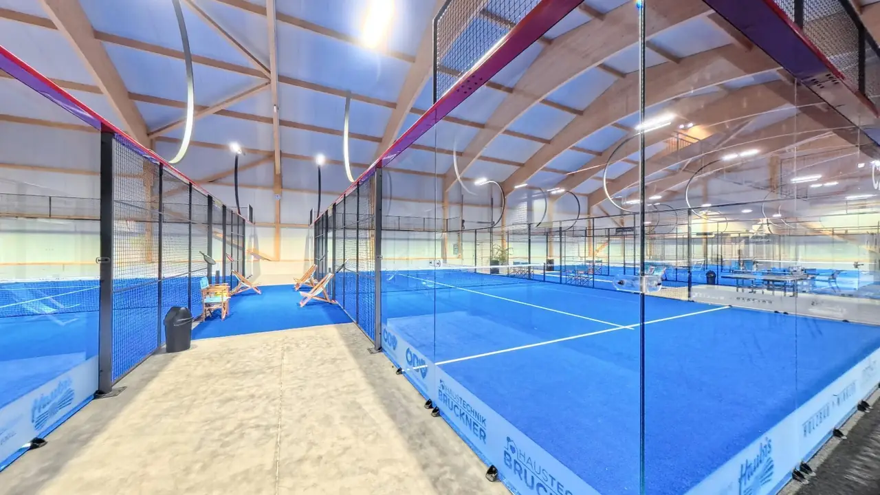 Blick in die Halle: Gang zwischen zwei blauen Courts unter der hohen Holzdachkonstruktion